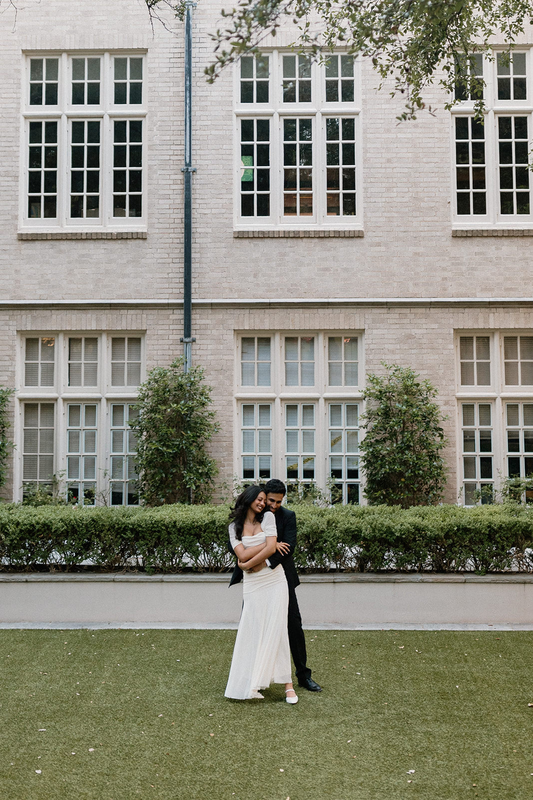 Angela and Ben embracing on the lawn beneath the church windows