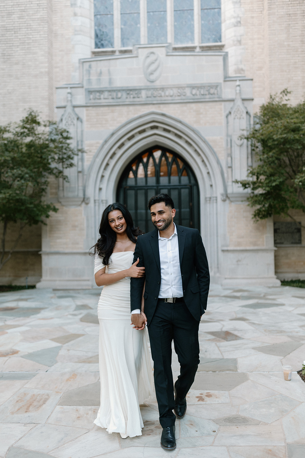Angela and Ben smiling as they walk hand in hand in front of the church